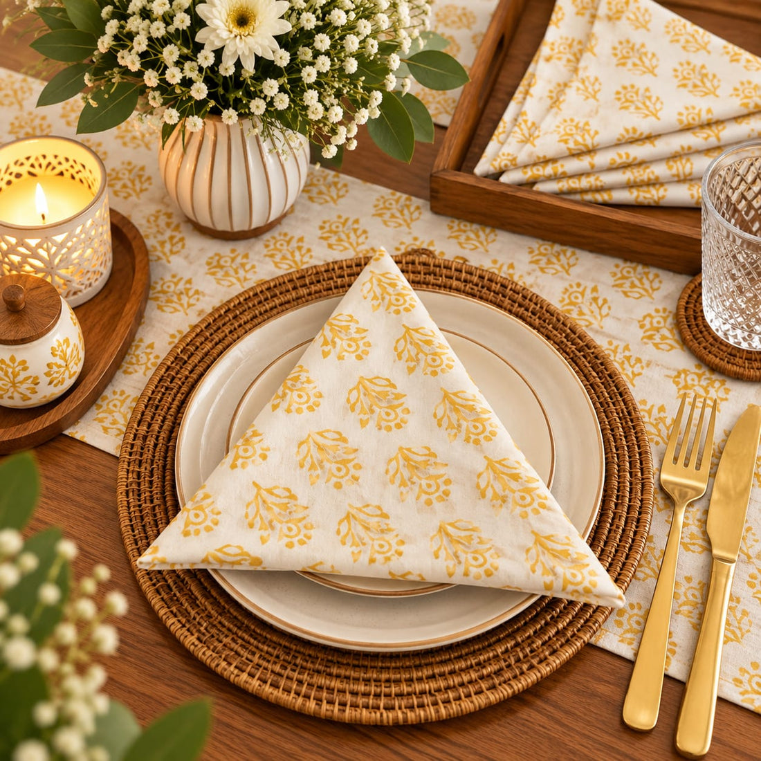 A rectangular placemat with a yellow and white geometric triangle pattern is displayed on a wooden table, surrounded by dining props including a glass, candle, flowers, and folded napkins.