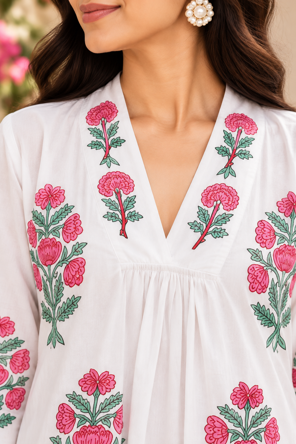 A close-up of a woman wearing a white long-sleeve top with vibrant pink floral embroidery and green leaves around a deep V-neckline.
