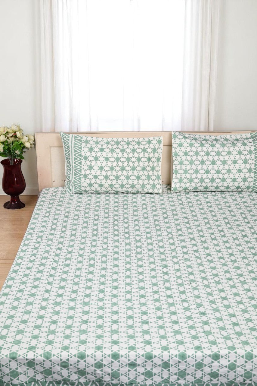 Bed with green and white patterned bedding and pillows, against a neutral background.