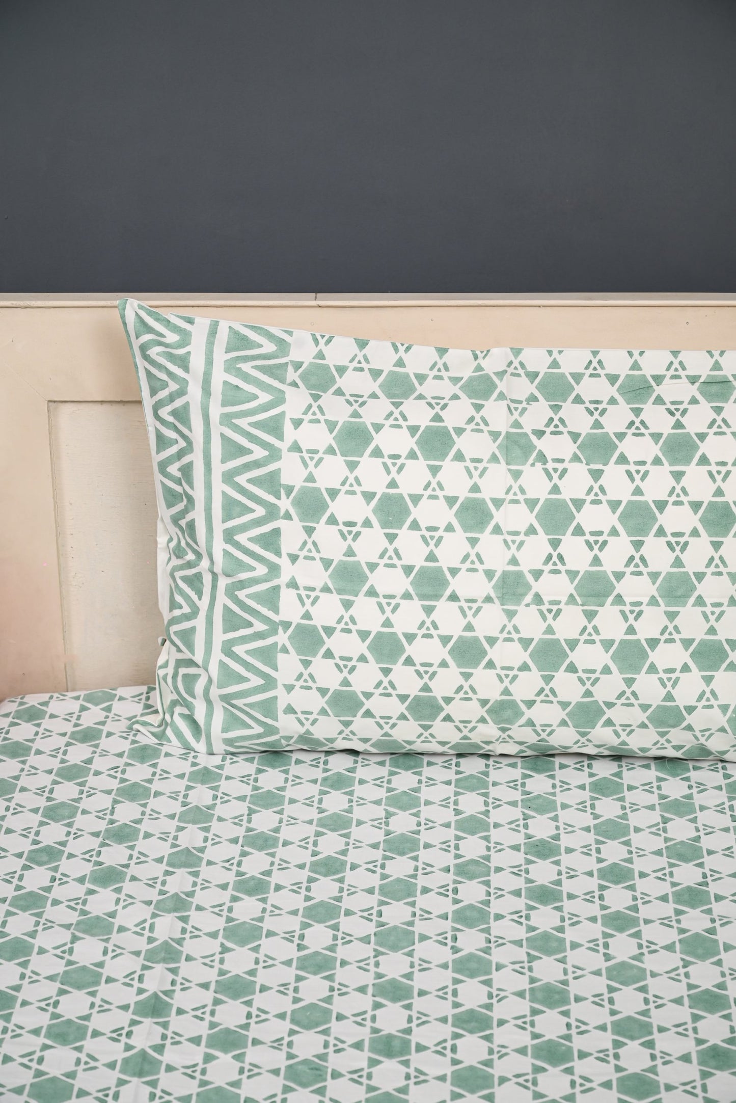 Bed with green geometric patterned bedding and pillow against a dark wall.