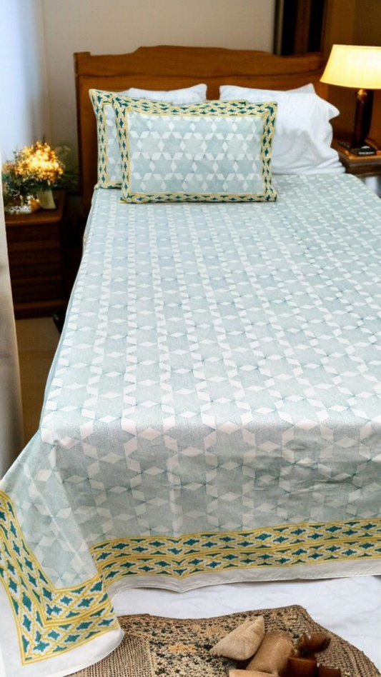 Bed with a light green quilt and matching pillows in a bedroom setting.