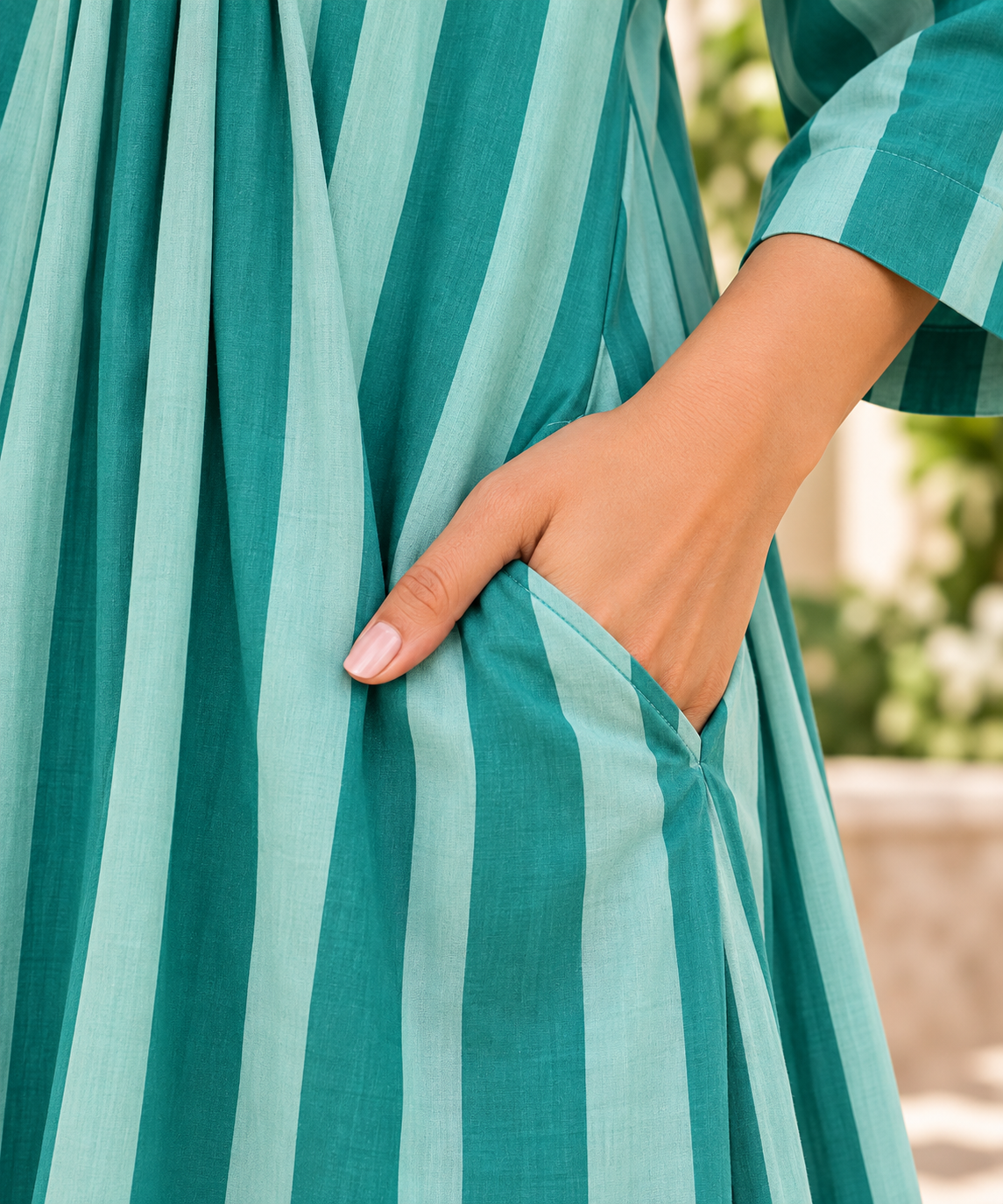 Close-up of a person wearing a teal and mint green vertically striped dress, with one hand tucked into a side pocket.
