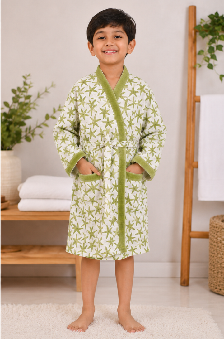 Child wearing a green and white patterned robe in a home setting with plants and towels.