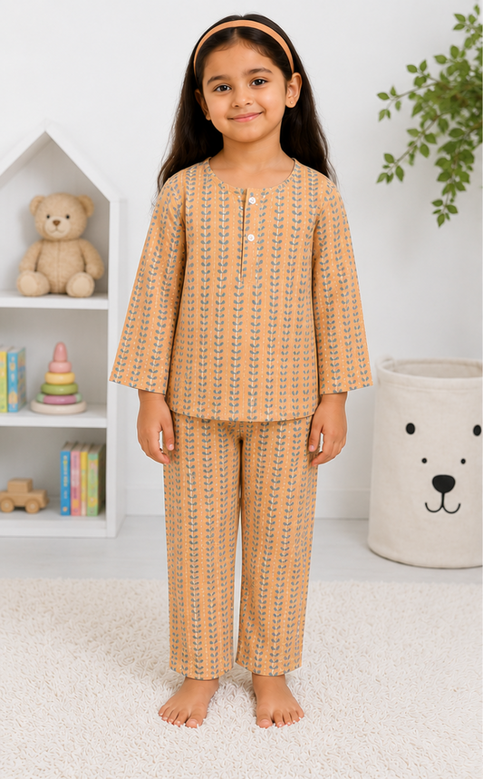 Young girl wearing a patterned pajama set in a room with a teddy bear and books in the background.